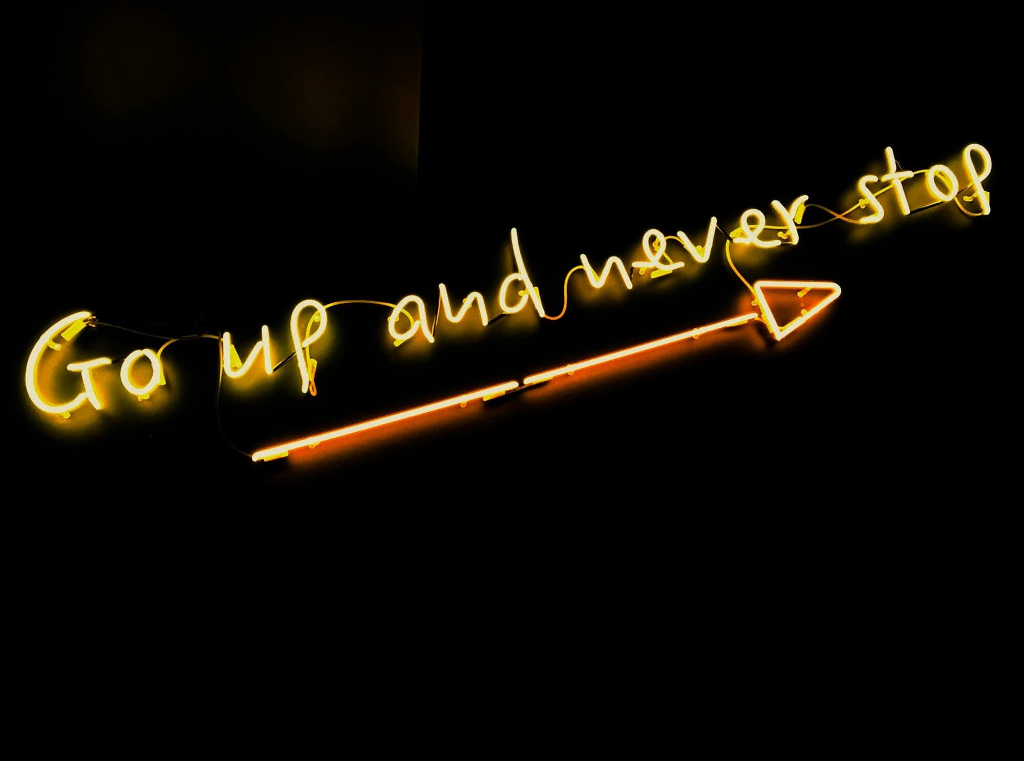 Neon sign saying Go Up and Never Stop